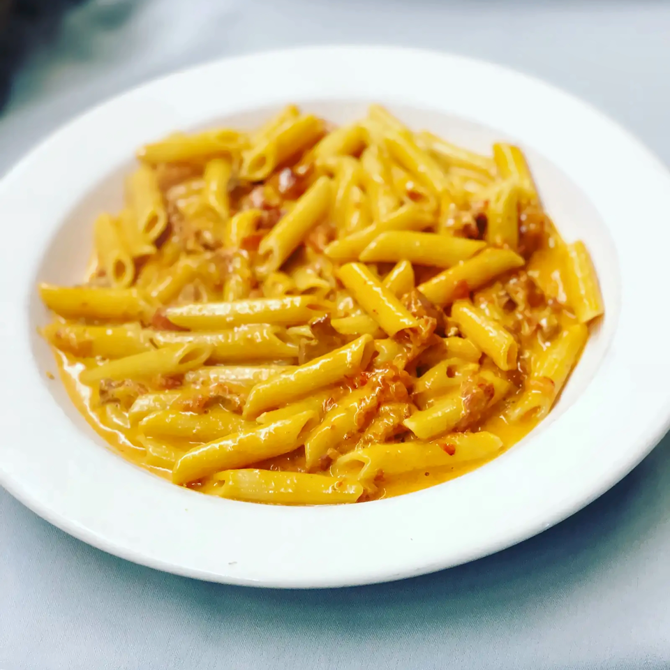 Plate of penne pasta coated in creamy orange sauce with visible bacon pieces.