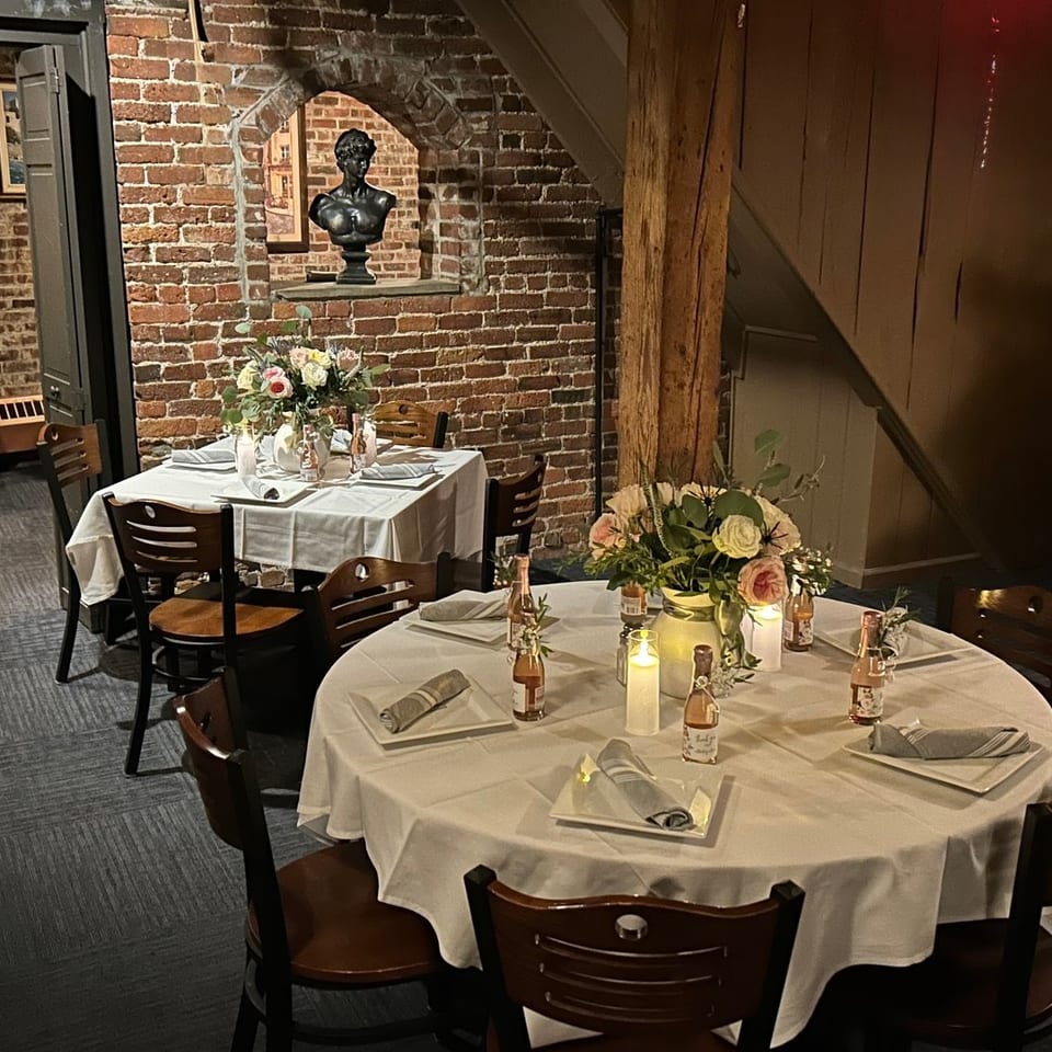 Two elegantly set dining tables with floral centerpieces and candles in a rustic brick-walled restaurant.